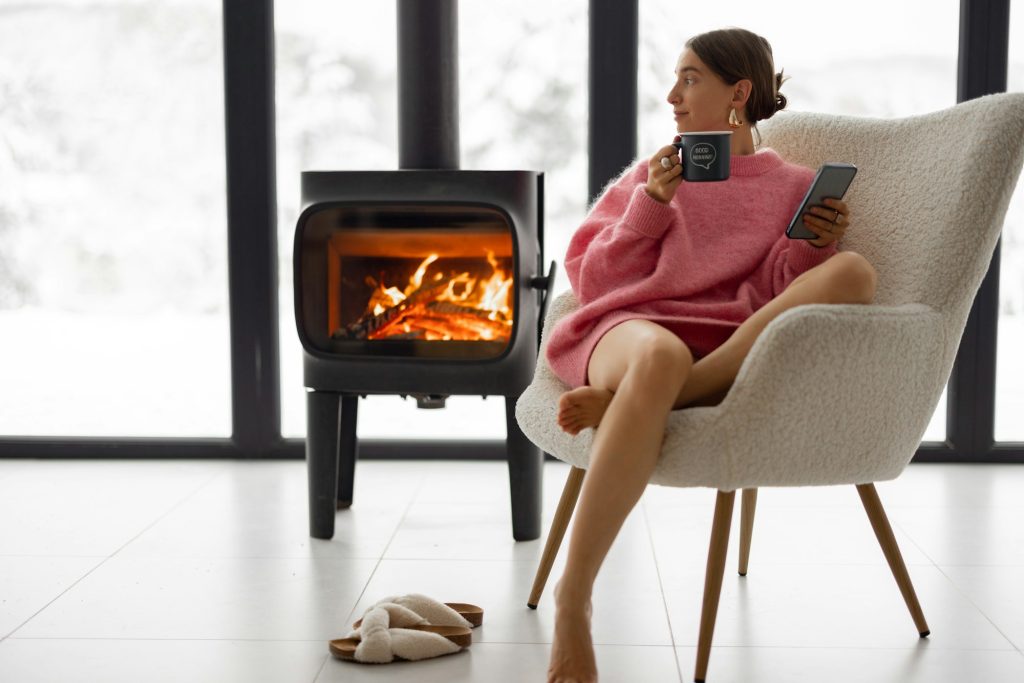 Woman with cup on chair by the fireplace at house on nature